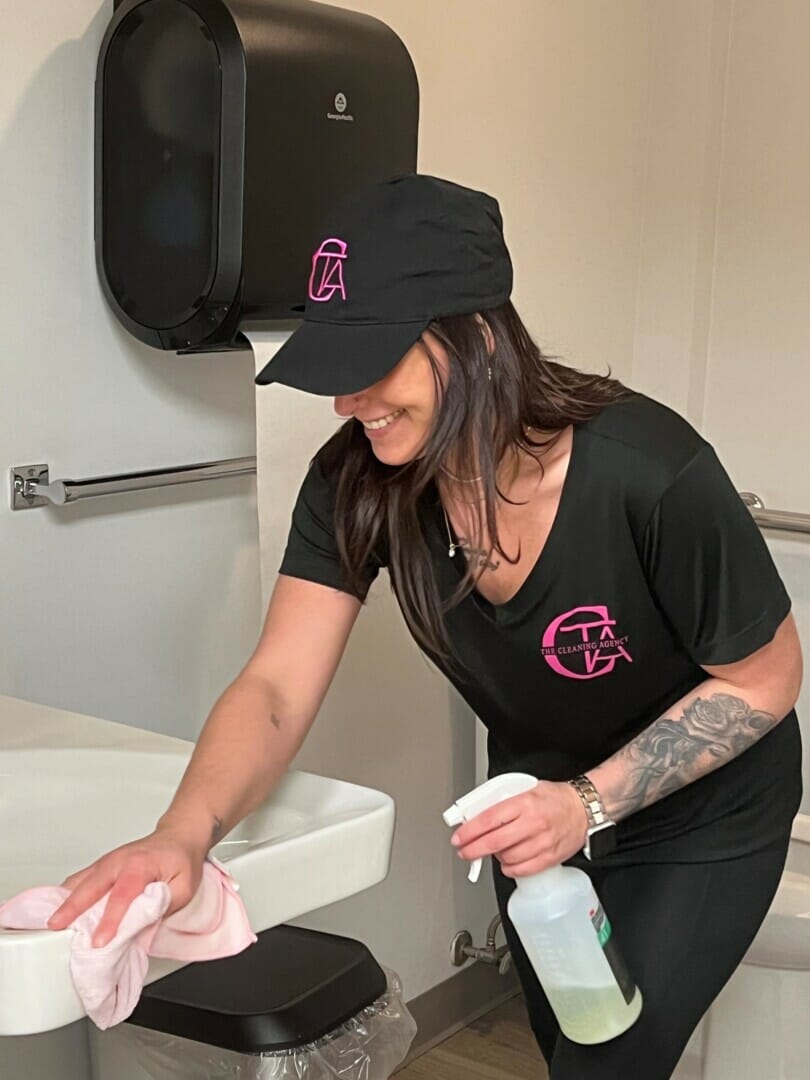 smiling cleaning lady disinfecting the bathroom sink